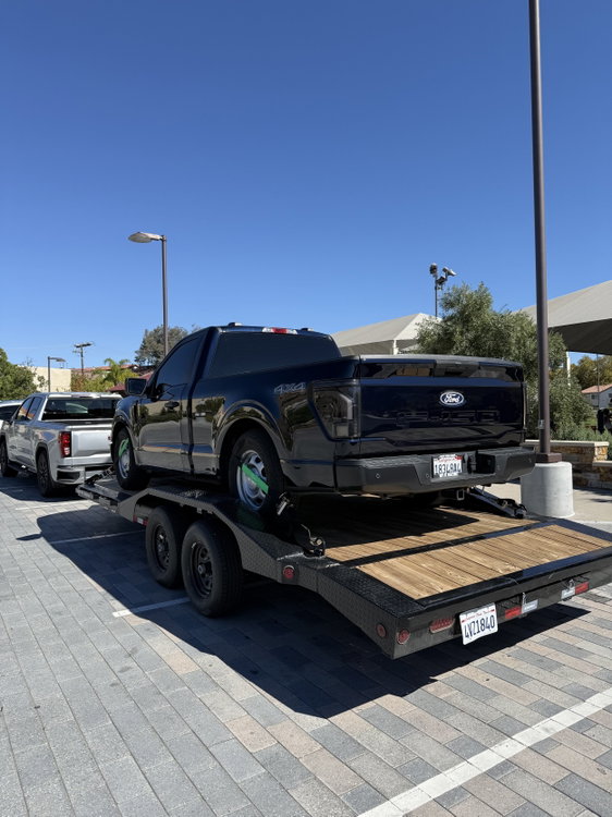 A rear view of a black Ford F-150 strapped onto our trailer, showing the low dovetail and wood deck that make loading easy.