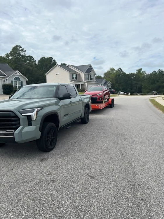 Pickup truck towing a red sedan on an orange car hauler trailer rented from Carson Rental Co.