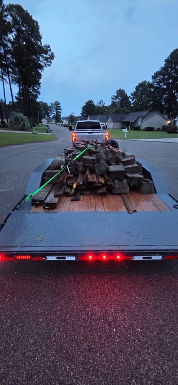 Black Lamar tandem-axle trailer rental hauling a ratchet-strapped load of old lumber and blocks in Raeford, NC