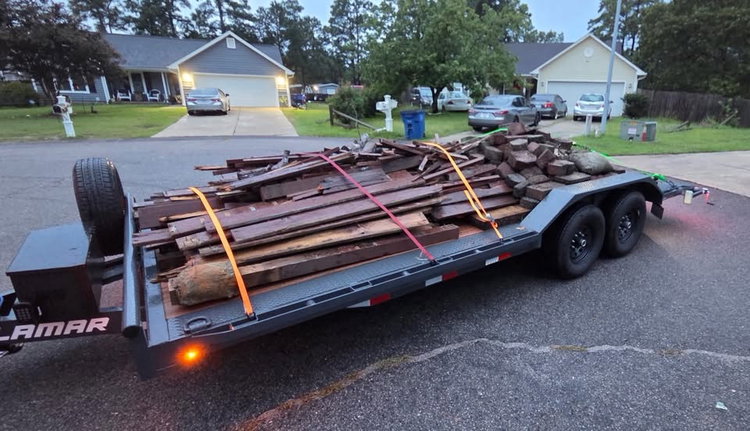 Black flatbed trailer rental loaded with strapped-down lumber and landscape blocks for a cleanup job at dusk