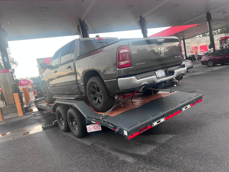 Grey pickup truck chained down on a black car hauler trailer rental from Carson Rental Co. at a fuel stop