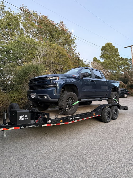 A lifted Chevy Silverado loaded and ratcheted down with wheel straps at all four corners. Our trailer handles full-size trucks with room to spare.